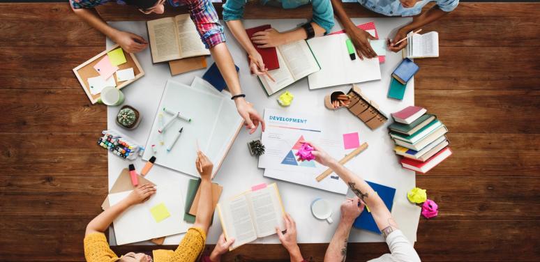 mess at a desk with people and books.