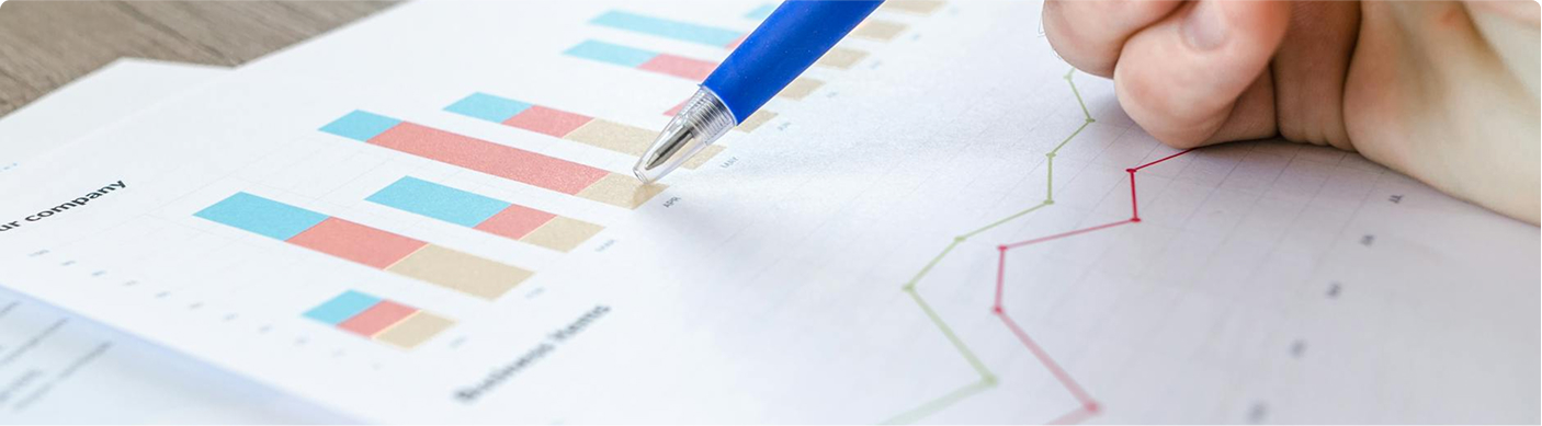 a hand with a pen hovers over papers with charts on it