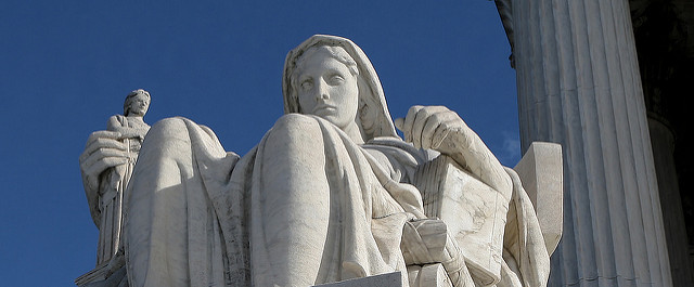 Statue of white stone depicts seated figure holding a small statue of a figure